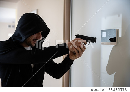 The hooded thief with a gun breaks into the apartment. The hooded thief with a gun breaks into the apartment. 73886538