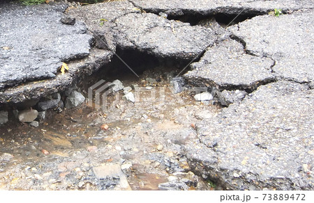 Water erosion of the road and red car. Broken asphalt background. Danger hole, stone gray backdrop Water erosion of the road and red car. Broken asphalt background. Danger hole, stone gray backdrop 73889472