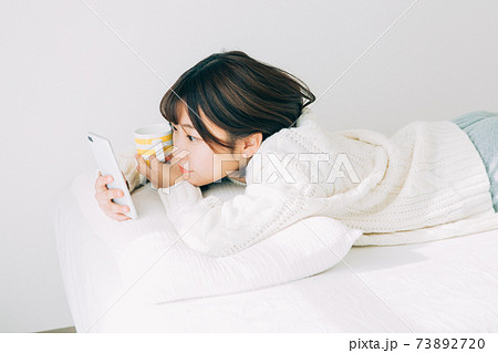 ベッドに寝転がってスマホを見る女性 73892720