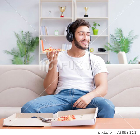 Man eating pizza having a takeaway at home relaxing resting Man eating pizza having a takeaway at home relaxing resting 73893111