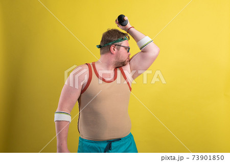 funny fat man doing exercises with dumbbells. Overweight. yellow background 73901850