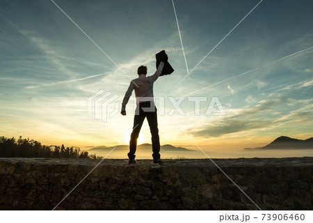Businessman holding aloft his jacket at sunset 73906460