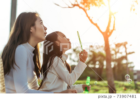 Happy asian mom and dougther in the garden, they are having fun playing and blowing bubbles. 73907481