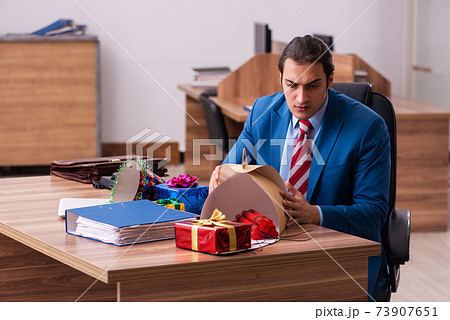 Young male employee celebrating Christmas at workplace Young male employee celebrating Christmas at workplace 73907651