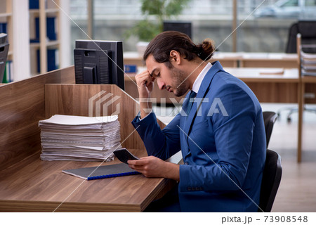 Young male employee unhappy with excessive work in the office Young male employee unhappy with excessive work in the office 73908548