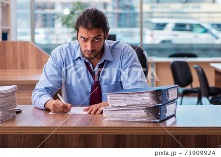 Young male employee unhappy with excessive work in the office Young male employee unhappy with excessive work in the office 73909924