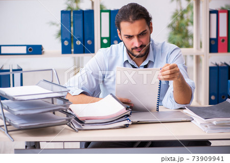 Young male employee unhappy with excessive work in the office Young male employee unhappy with excessive work in the office 73909941