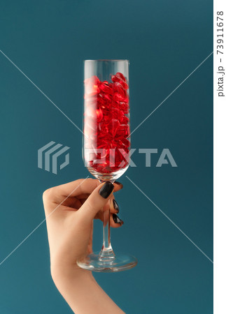 Beautiful card with female hand holding champagne glass filled with transparent red hearts on dark aqua backdrop. Love and celebration concept. Great design for any purposes. 73911678