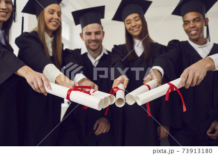 Graduates friends joining diplomas together as symbol of unity, common achievement, team, success Graduates friends joining diplomas together as symbol of unity, common achievement, team, success 73913180