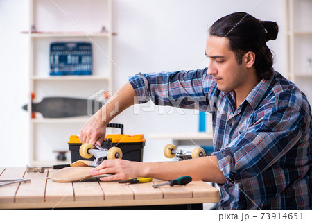 Young man repairing skateboard at workshop 73914651