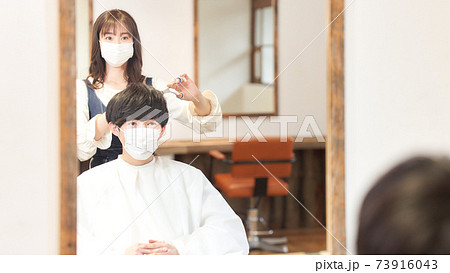 ヘアカットをするマスク着用の女性店員とお客の写真素材