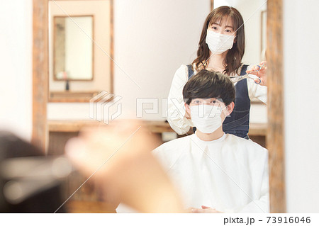 ヘアカットをするマスク着用の女性店員とお客の写真素材