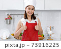Portrait of happy Asian woman chef in red apron standing in kitchen. 73916225