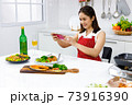 Asian woman in red apron taking a picture of food she make with mobile phone. Concept woman preparing meals at home. 73916390