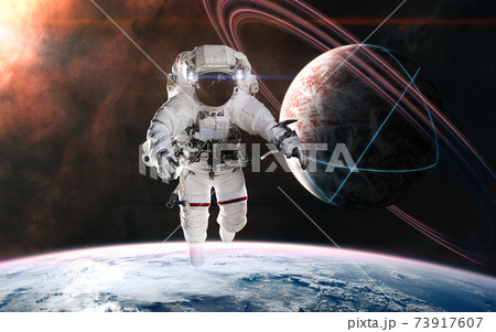 Astronaut on background of planets in deep space. Glowing structures on surface of planet with rings 73917607