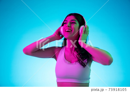 Brunette beautiful woman's portrait isolated on blue studio background in multicolored neon light Brunette beautiful woman's portrait isolated on blue studio background in multicolored neon light 73918105