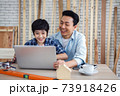 Asian father and son using laptop computer together in carpentry workshop. Concept family doing hobby at home. 73918426