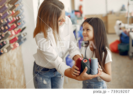 Mother with little daughter standing at the fabric with thread Mother with little daughter standing at the fabric with thread 73919207