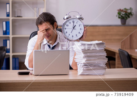 Young male employee in time management concept in the office Young male employee in time management concept in the office 73919409