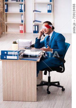Blindfolded male employee working in the office Blindfolded male employee working in the office 73919466