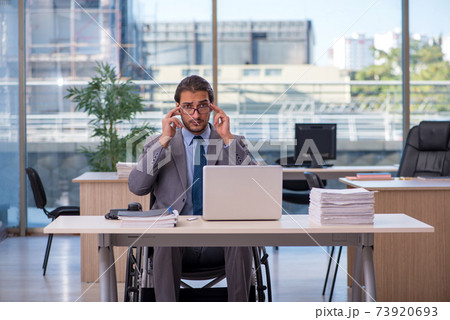 Young male employee in wheel-chair working in the office Young male employee in wheel-chair working in the office 73920693