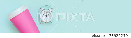 Simply flat lay design pink paper coffee cup and alarm clock isolated on blue pastel background. Takeaway drink breakfast beverage. Good morning wake up awake concept. Top view copy space, banner 73922259