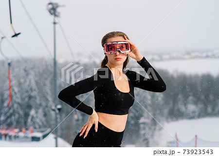 Female in sport wear snowboarder posing in sunglasses with snowboard 73923543