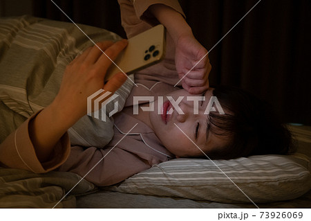 眠いのに布団でスマホを見る女性 眠いのに布団でスマホを見る女性 73926069