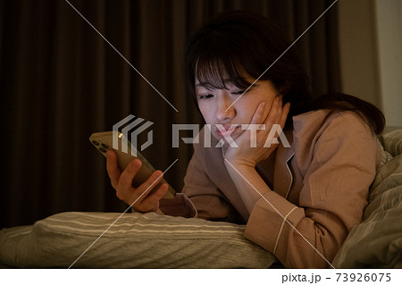 暗い部屋でスマホを見て落ち込む女性の写真素材