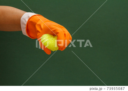 Woman's hand in protective glove with sponge on the green background. 73935087