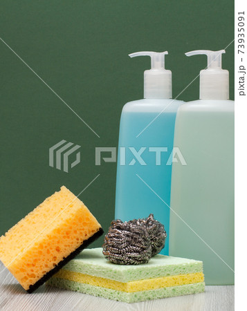 Bottles of dishwashing liquid, glass and tile cleaner and sponges on green background. 73935091