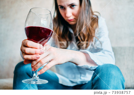 A drunk girl drinks wine and looks at a glass while sitting on a sofa. 73938757