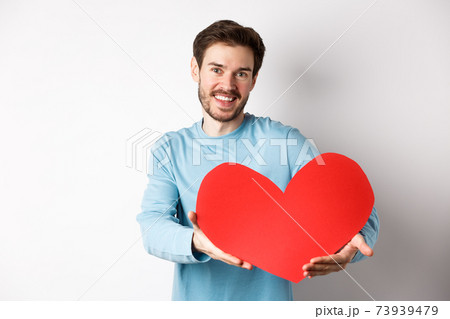 Happy gay man giving big red heart to his lover on valentines day, concept of romantic date and love celebration, standing over white background Happy gay man giving big red heart to his lover on valentines day, concept of romantic date and love celebration, standing over white background 73939479