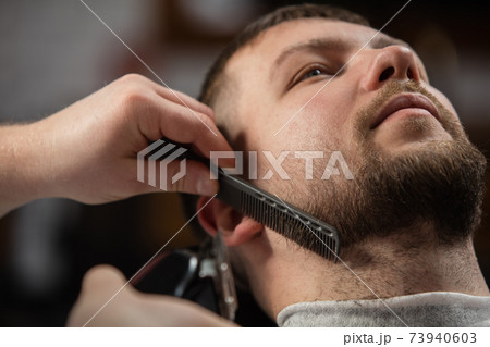 Close up of client of master barber, stylist during getting care of mustache and beard. Professional occupation, male beauty concept 73940603