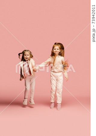 Happy kids, girls isolated on coral pink studio background. Look happy, cheerful, sincere. Copyspace. Childhood, education, emotions concept Happy kids, girls isolated on coral pink studio background. Look happy, cheerful, sincere. Copyspace. Childhood, education, emotions concept 73942011