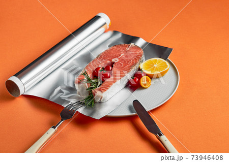 fresh salmon with lemon in foil paper, ready for cooking in oven on orange background 73946408