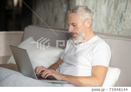 Serious man working on laptop in bed Serious man working on laptop in bed 73948144