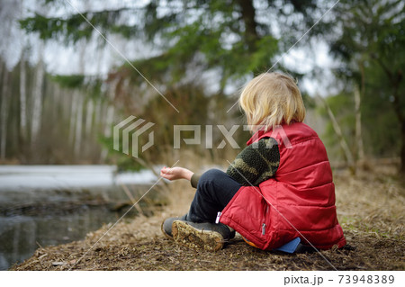 Little boy relaxing on shore of forest lake on early springtime Little boy relaxing on shore of forest lake on early springtime 73948389