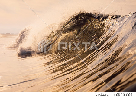 Glassy wave at sunrise. Breaking ocean wave with warm colors, swell for surfing 73948834