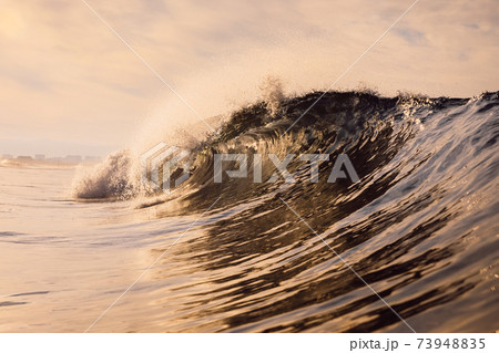 Glassy wave at sunrise. Breaking ocean wave with warm colors, swell for surfing 73948835