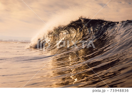 Glassy wave at sunrise. Breaking ocean wave with warm colors, swell for surfing 73948836