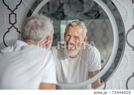 Smiling grey-haired man looking at the mirror Smiling grey-haired man looking at the mirror 73948929