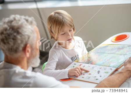 Boy reading an interesting book together with his father 73948941