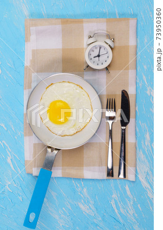 Alarm clock and frying pan fried egg with fork and knife. The concept of Breakfast. vertical photo Alarm clock and frying pan fried egg with fork and knife. The concept of Breakfast. vertical photo 73950360