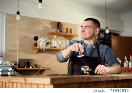 Barista presses ground coffee using tamper in a coffe shop Barista presses ground coffee using tamper in a coffe shop 73950950