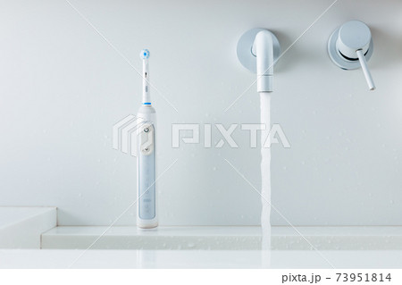 electric toothbrush on a wash-bowl, water flowing from faucet 73951814