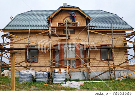 The house made of foam concrete, insulated with mineral wool and lined with facade brick, has a scaffolding near the house. The house made of foam concrete, insulated with mineral wool and lined with facade brick, has a scaffolding near the house. 73953639