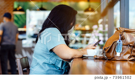 Mini alcohol gel bottle to kill Corona Virus(Covid-19) hang on a brown leather shoulder bag with hot coffee on table in cafe.New normal lifestyle.Health care concept.Selective focus on alcohol gel 73961502