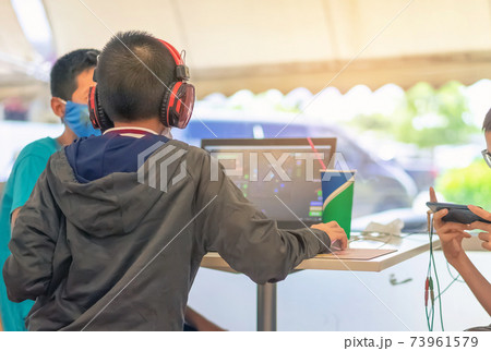 Back view of Asian boy wearing protective face mask and headphones while working with a friend on laptop during corona virus (Covid-19) and flu outbreak in food court at the mall.New normal lifestyle. Back view of Asian boy wearing protective face mask and headphones while working with a friend on laptop during corona virus (Covid-19) and flu outbreak in food court at the mall.New normal lifestyle. 73961579