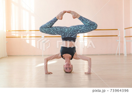 Flexible Caucasian girl stands on her head in a dance class. The girl does yoga. . Woman dancing breakdance on the background of ballet barre. Flexible Caucasian girl stands on her head in a dance class. The girl does yoga. . Woman dancing breakdance on the background of ballet barre. 73964396